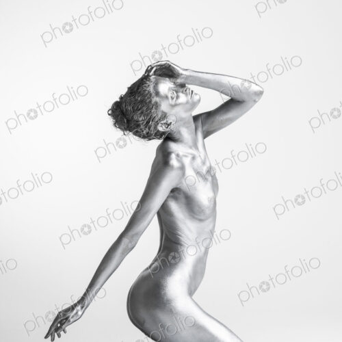 Nude Caucasian woman with silver body paint kneeling, side view hand on head Nude Caucasian woman with silver body paint kneeling, side view hand on head