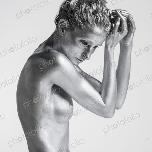 Nude Caucasian woman with silver body paint side view, hands to head Nude Caucasian woman with silver body paint side view, hands to head