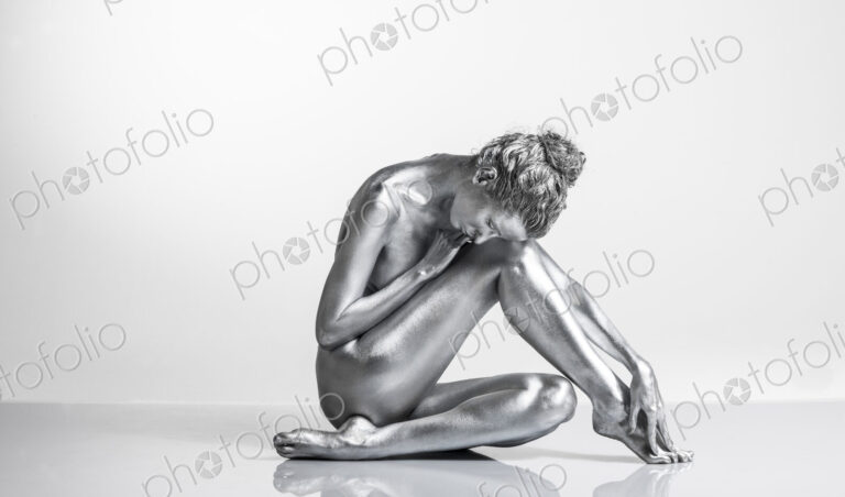 Nude Caucasian woman with silver body paint sitting