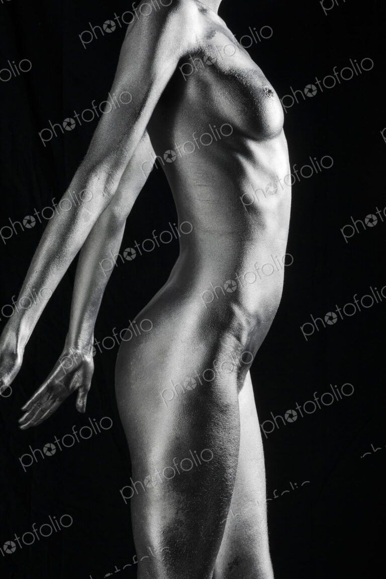 Nude Caucasian woman with silver body paint standing, side view