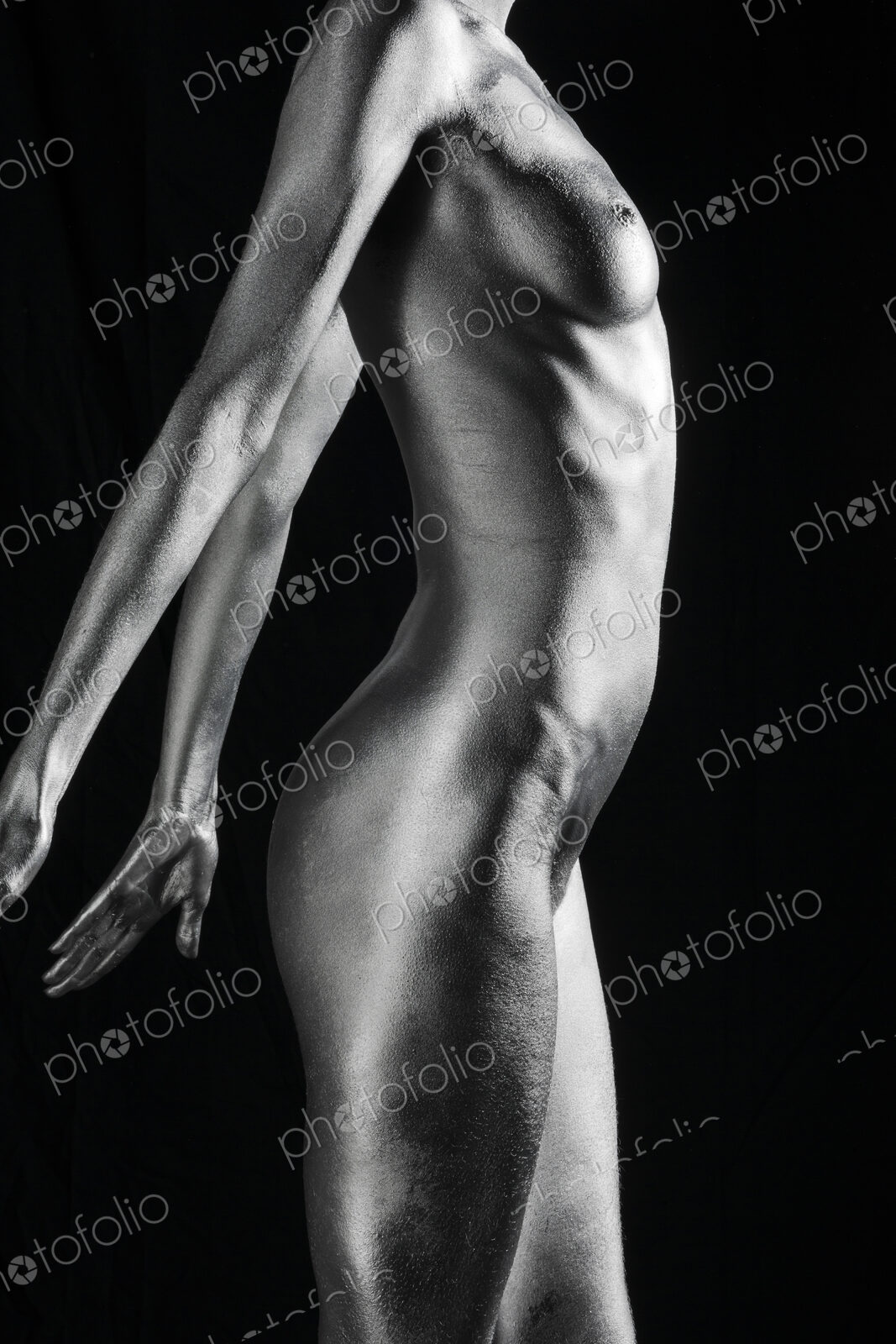 Nude Caucasian woman with silver body paint standing, side view