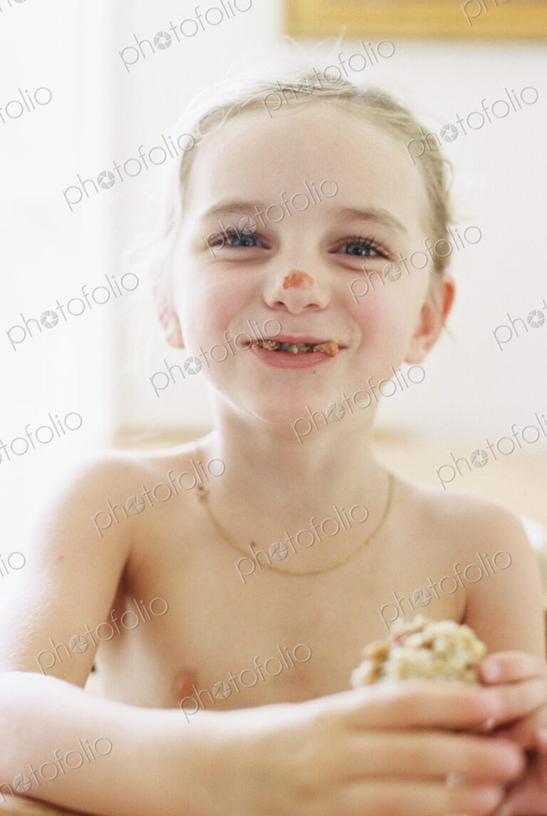 Nude young girl eating a sandwich, with crumbs in her mouth and tomato sauce on her…
