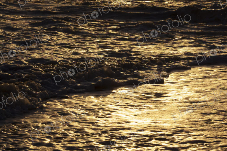 Ocean waves breaking on the shore at sunset, light reflecting off the water.