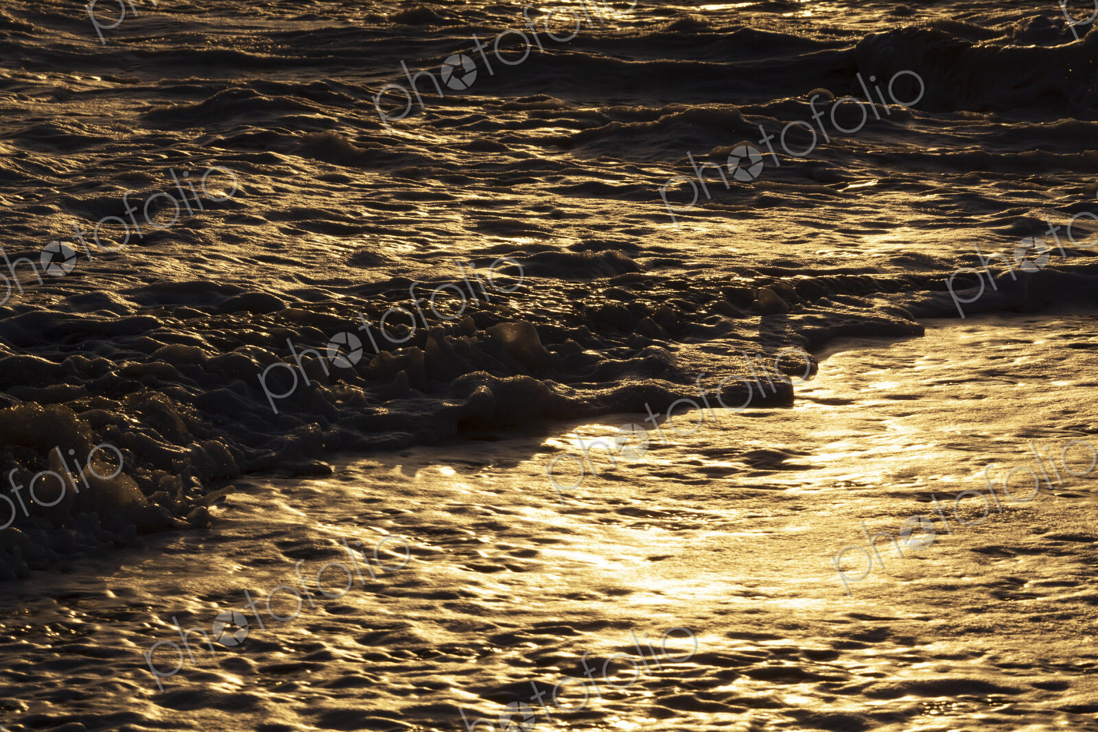 Ocean waves breaking on the shore at sunset, light reflecting off the water.