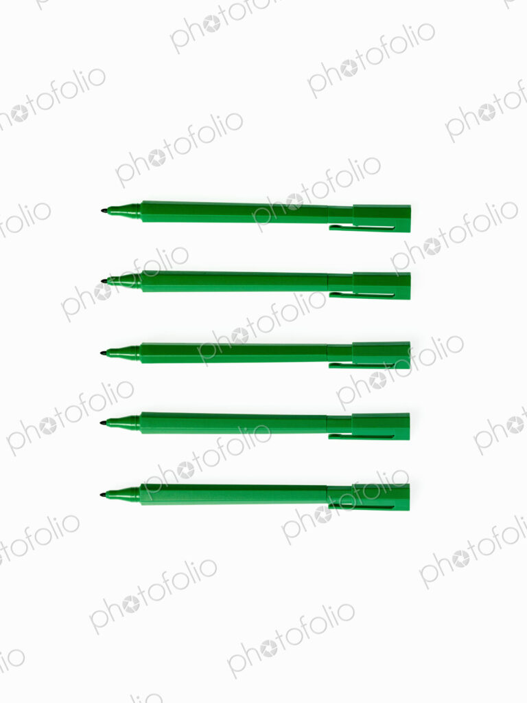 Office supplies. Green coloured pens, felt nibs and pen top cases, arranged in a row.