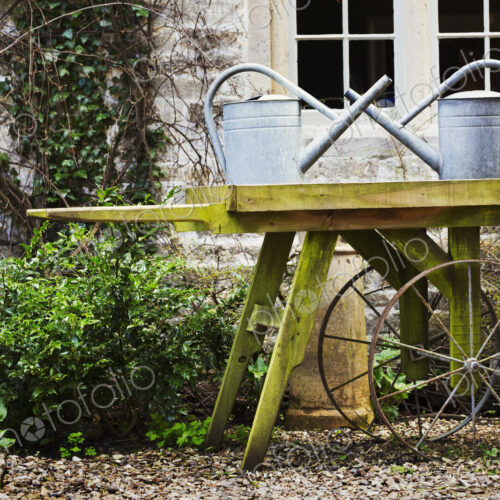 Old fashioned wooden wheel barrow and tin watering cans in the garden of an old house. Old fashioned wooden wheel barrow and tin watering cans in the garden of an old house.