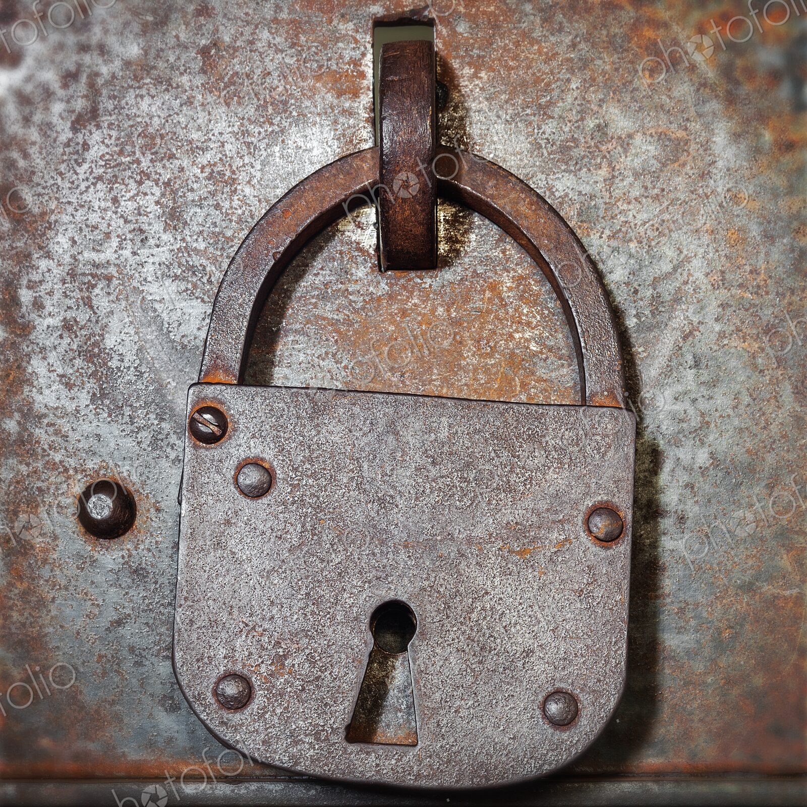 Old iron padlock hangs on a weathered metal door with rivets and rust, evoking…