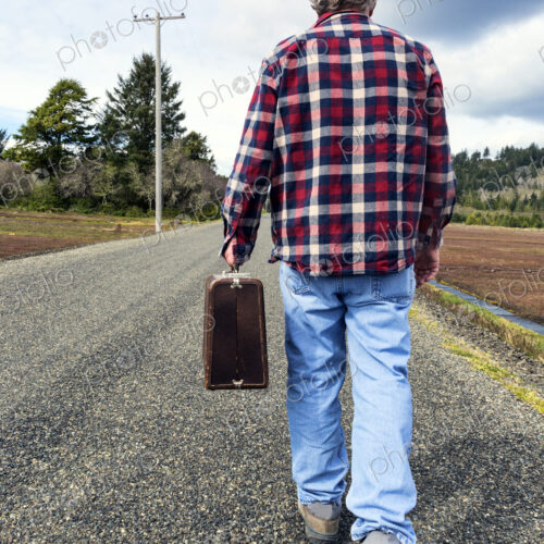 Older man carrying suitcase on rural road