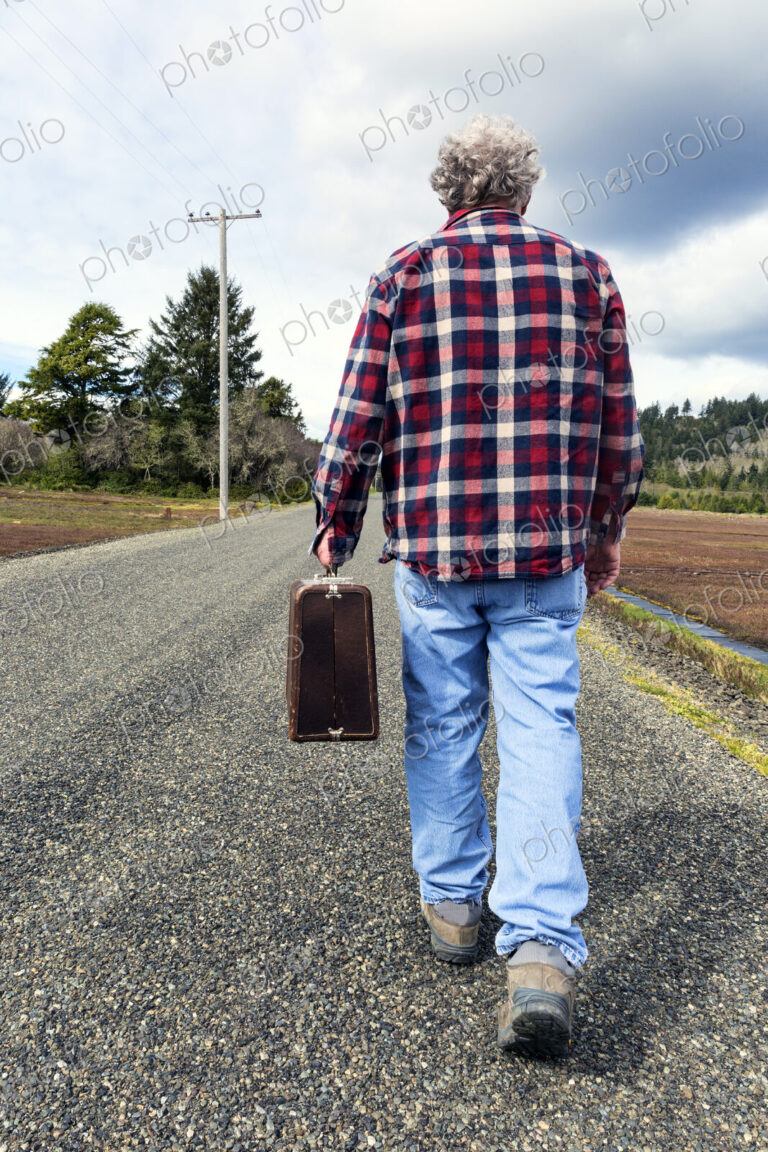 Older man carrying suitcase on rural road