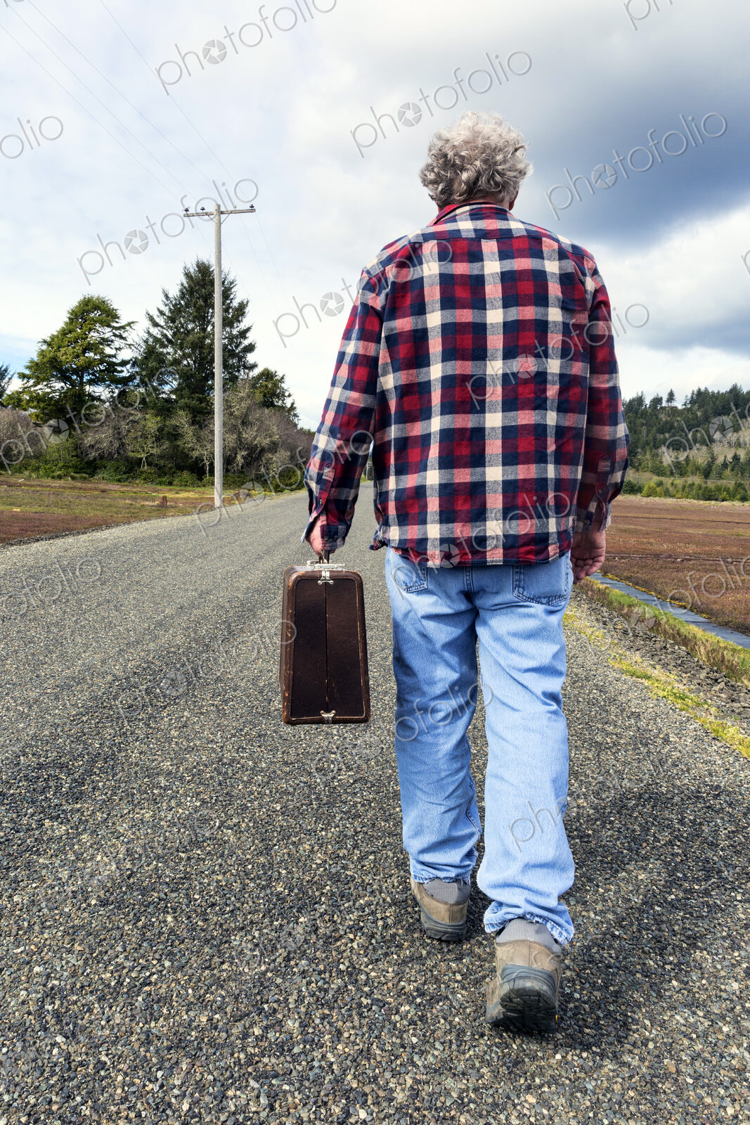 Older man carrying suitcase on rural road