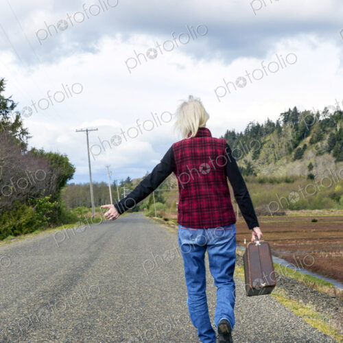 Older woman hitch hiking on rural road