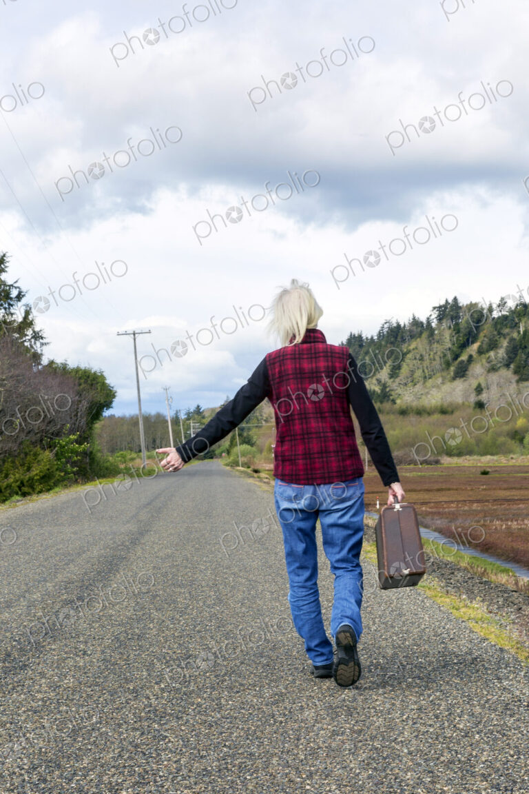 Older woman hitch hiking on rural road
