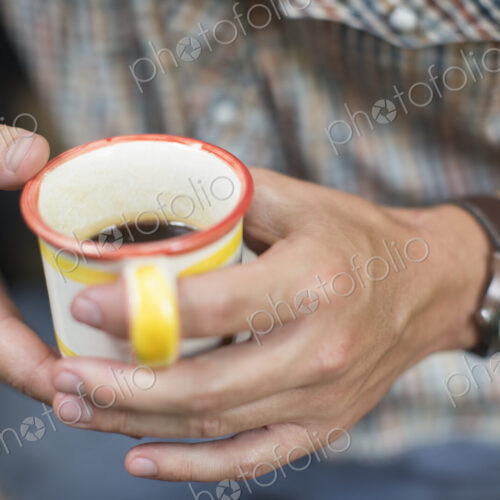 One person at a picnic table outdoors, holding a china mug.