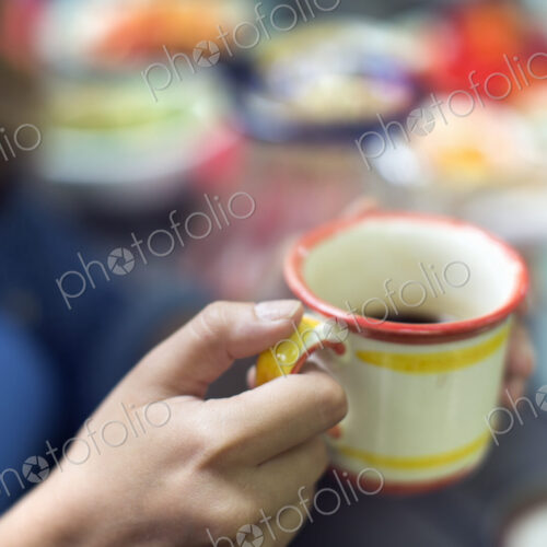 One person at a picnic table outdoors, holding a china mug. One person at a picnic table outdoors, holding a china mug.