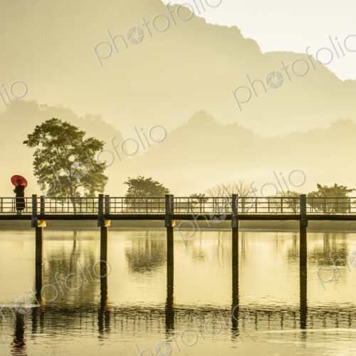 One person on a footbridge above water, mountains in the mist at dawn. One person on a footbridge above water, mountains in the mist at dawn.