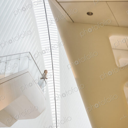 One person standing on a floating suspended balcony in the open space of a white atrium