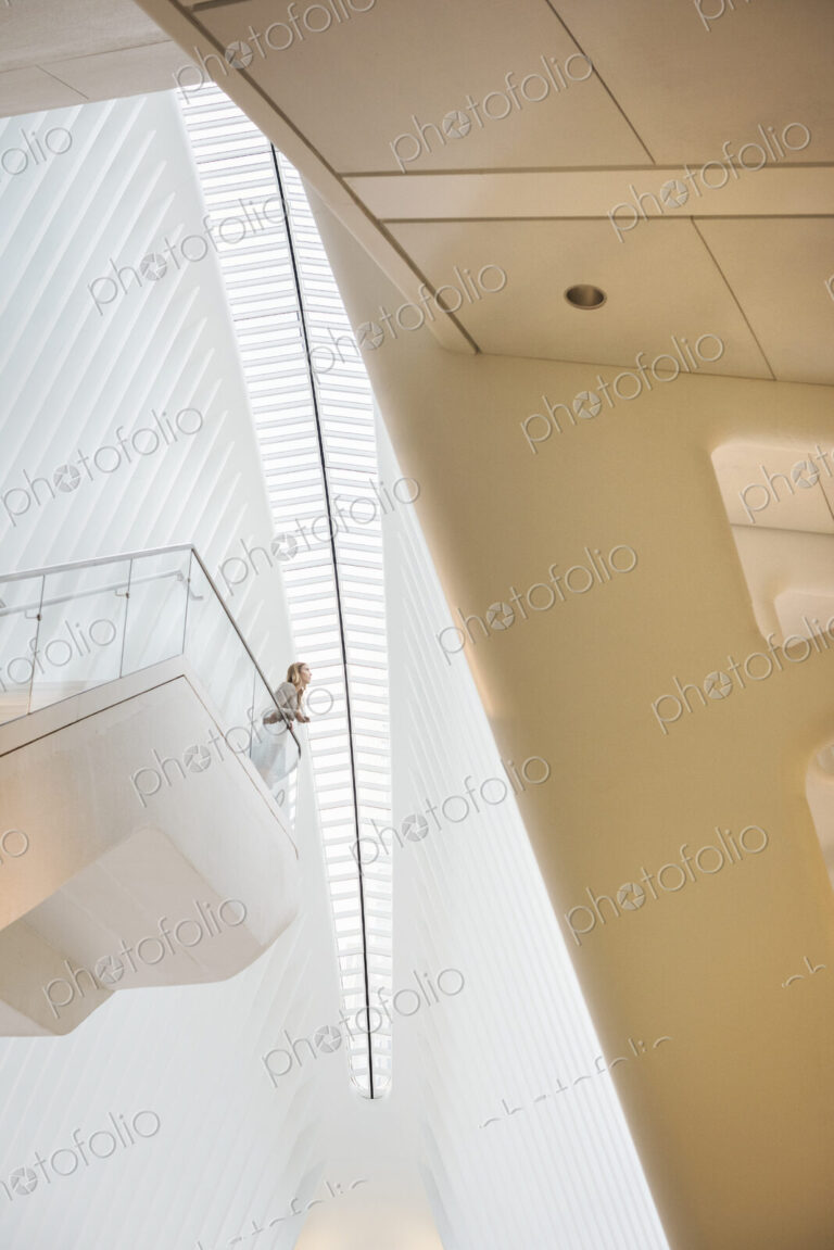One person standing on a floating suspended balcony in the open space of a white atrium