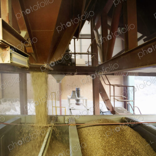 Open chutes pouring biomass fuel pellets into a hopper., Biomass fuel producer.