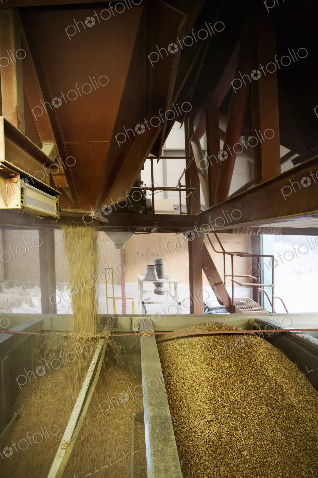 Open chutes pouring biomass fuel pellets into a hopper., Biomass fuel producer.