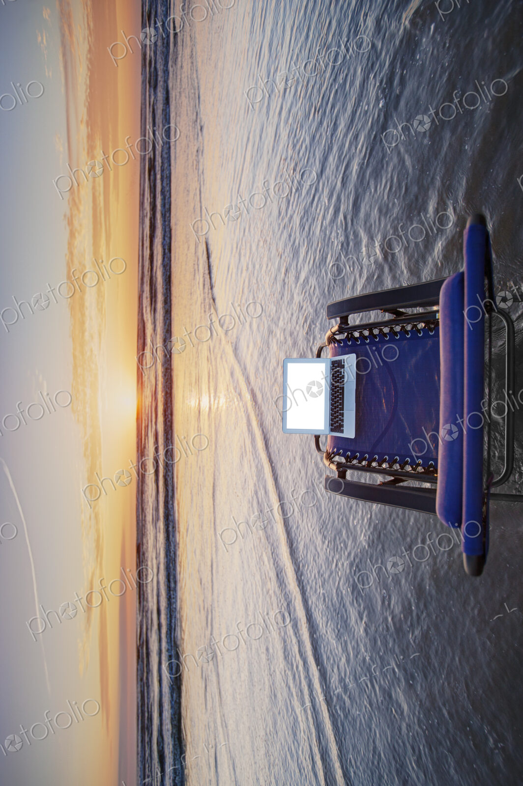 Open laptop on sun lounger in shallow wave at beach at sunset.