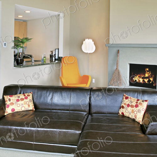 Open plan living room and kitchen in a modern home, a lit fire and sectional sofa.