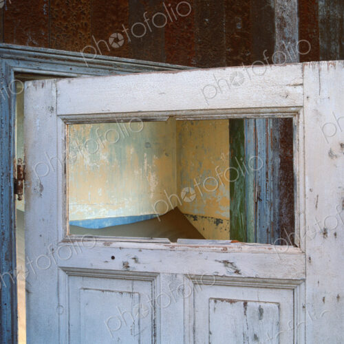 Open wooden door in a building buried in sand.