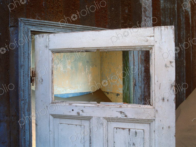 Open wooden door in a building buried in sand.