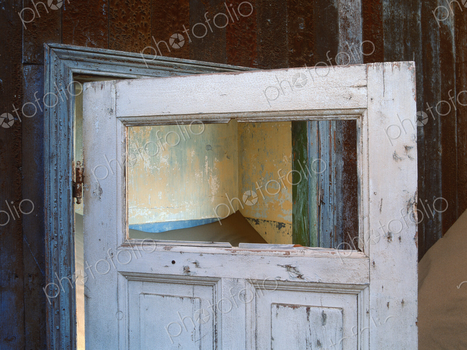 Open wooden door in a building buried in sand.
