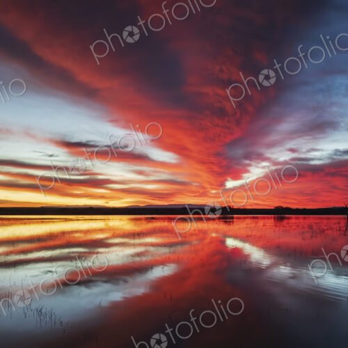 Orange and yellow glow on the horizon at sunset, reflected in a flat calm water…