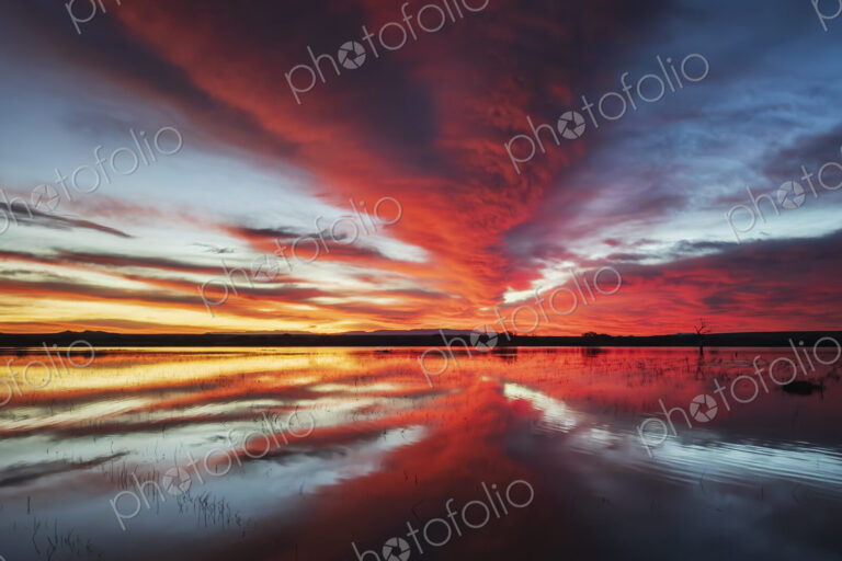 Orange and yellow glow on the horizon at sunset, reflected in a flat calm water…
