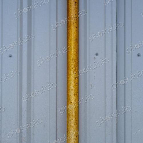 Orange gutter drain pipe against corrugated metal warehouse wall, close up