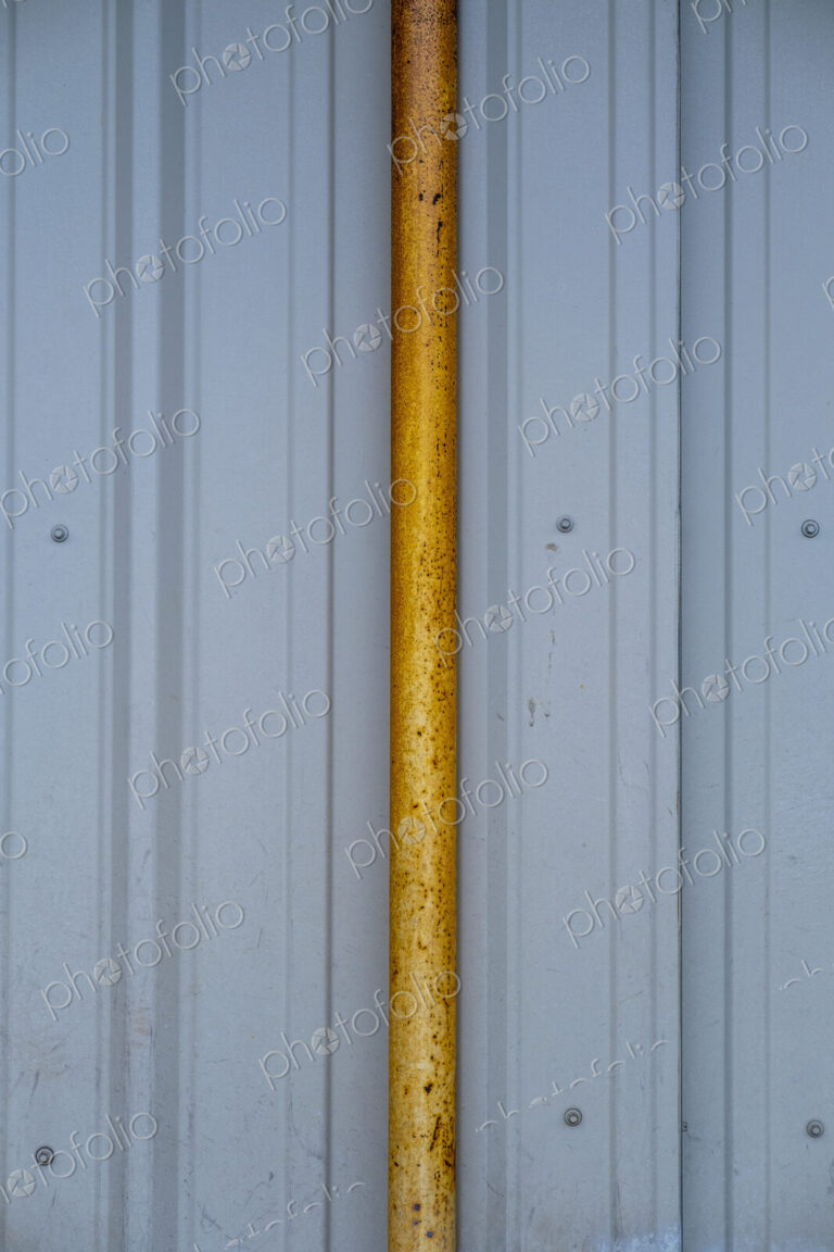Orange gutter drain pipe against corrugated metal warehouse wall, close up