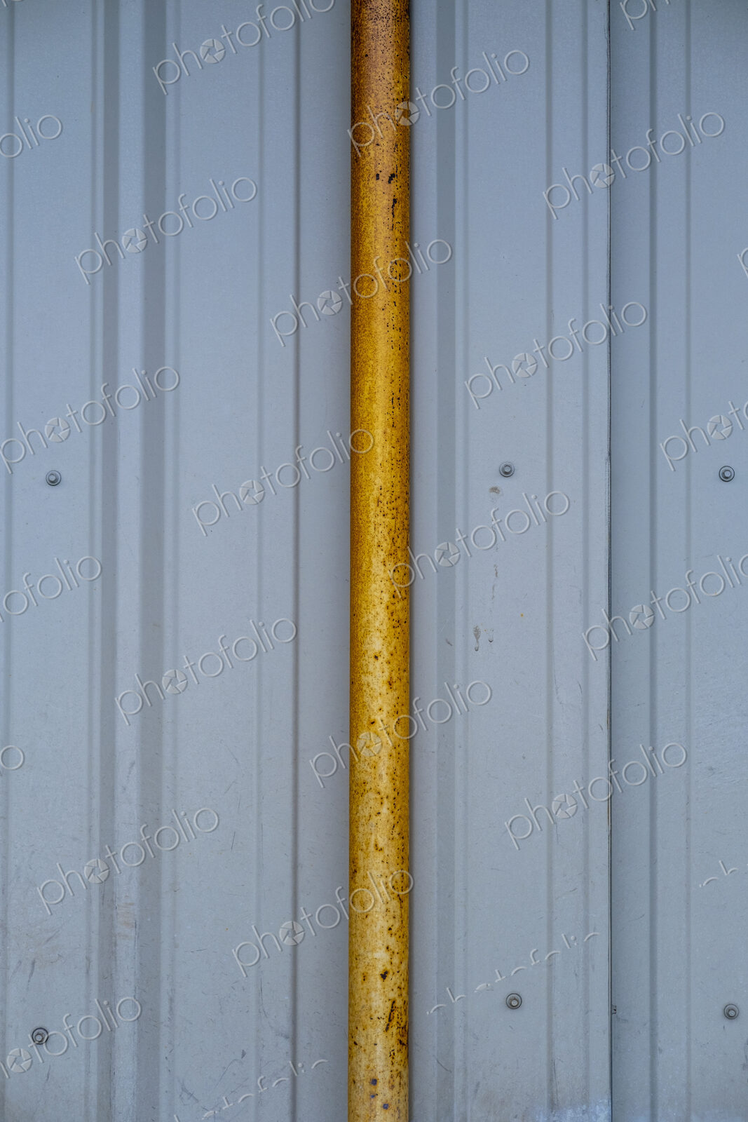 Orange gutter drain pipe against corrugated metal warehouse wall, close up