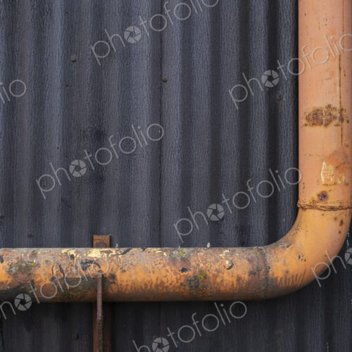 Orange gutter drain pipe against warehouse wall, close up Orange gutter drain pipe against warehouse wall, close up