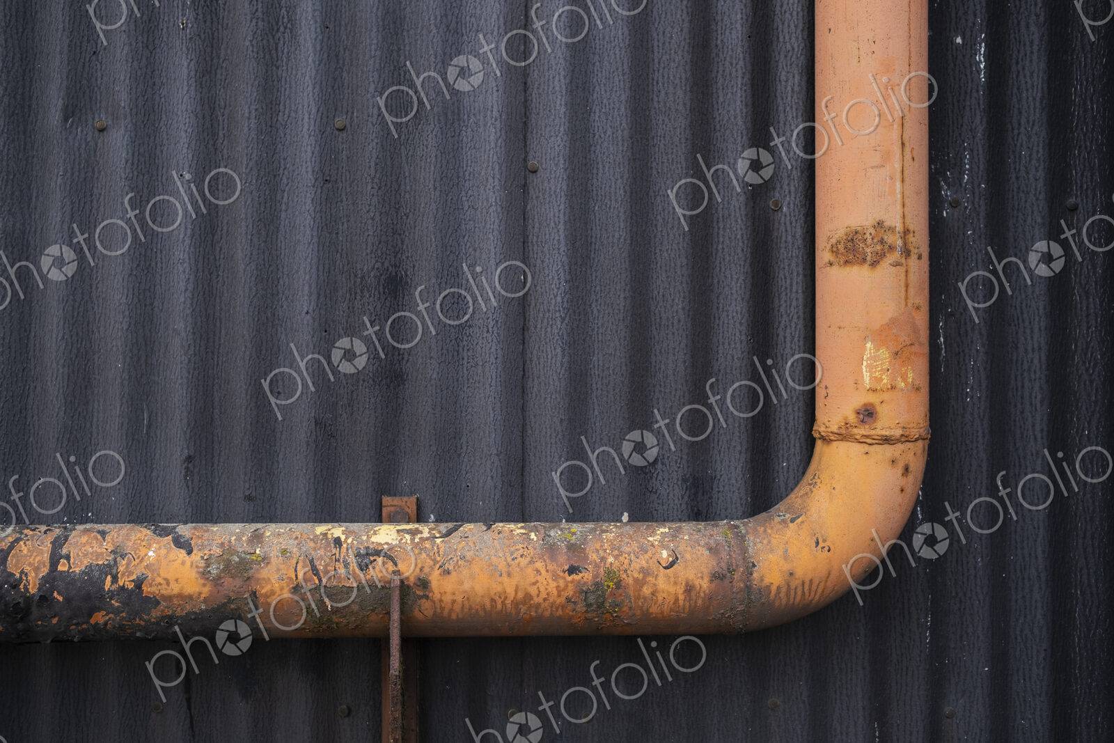 Orange gutter drain pipe against warehouse wall, close up