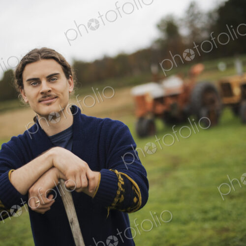 Organic Farmer at Work, A man leaning on a garden hoe. A tractor in the background. Organic Farmer at Work, A man leaning on a garden hoe. A tractor in the background.