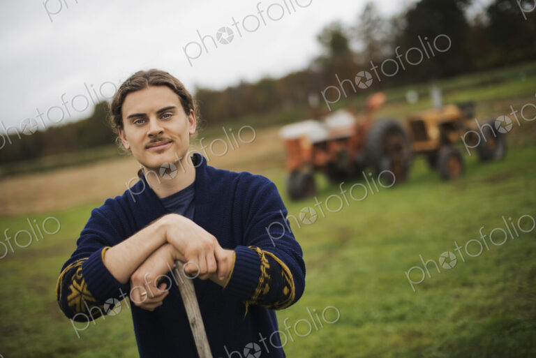 Organic Farmer at Work, A man leaning on a garden hoe. A tractor in the background.