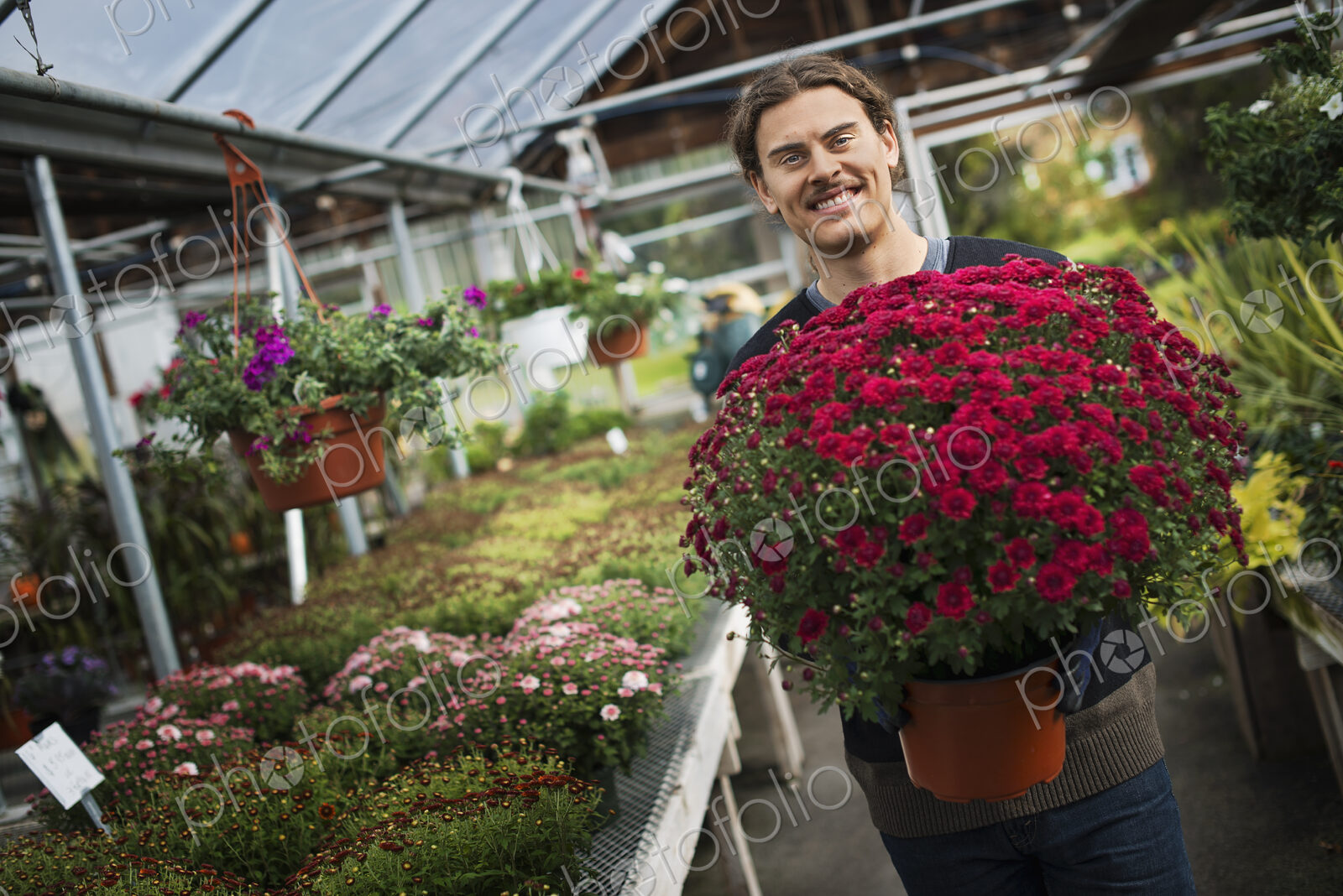 Organic Farmer at Work. A young man holding a large pot of flowering plants.