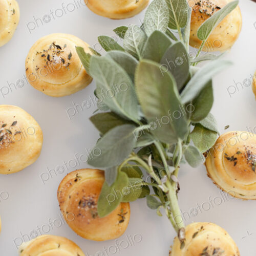 Organic dinner bread rolls on a white board with salt and sage garnish