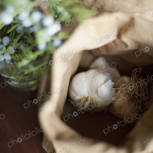 Organic ingredients on a table. Garlic bulbs in a brown paper bag. A herb with with…