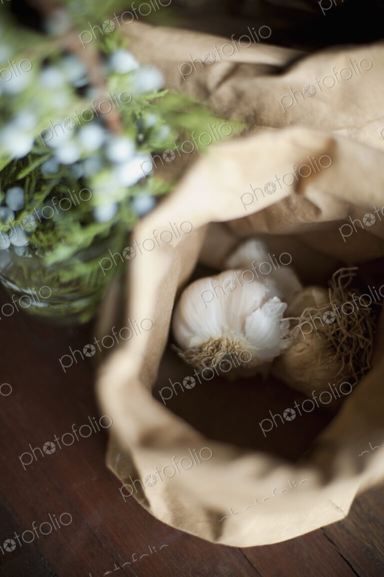 Organic ingredients on a table. Garlic bulbs in a brown paper bag. A herb with with…