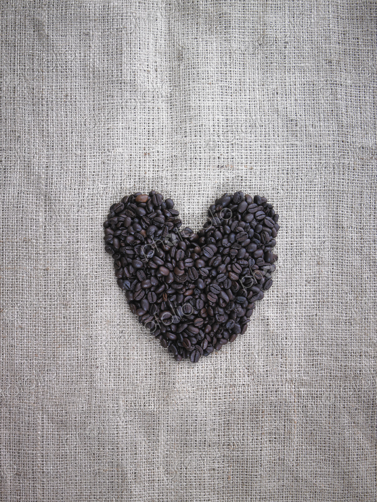 Organic roasted coffee beans in a heart shape on a burlap sack.