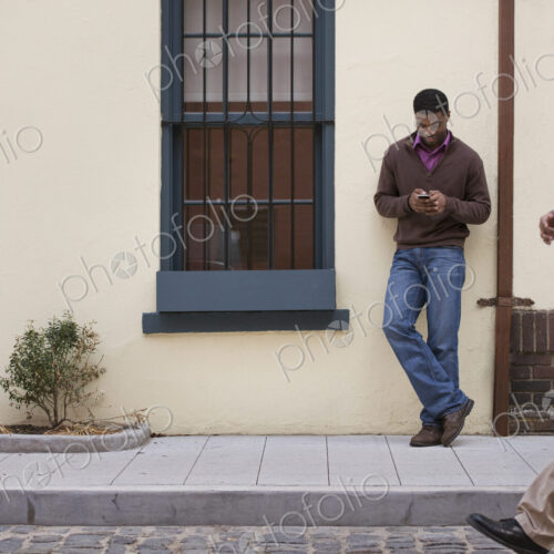 Outdoors in the city in spring. A couple walking on the sidewalk, and a man leaning… Outdoors in the city in spring. A couple walking on the sidewalk, and a man leaning…