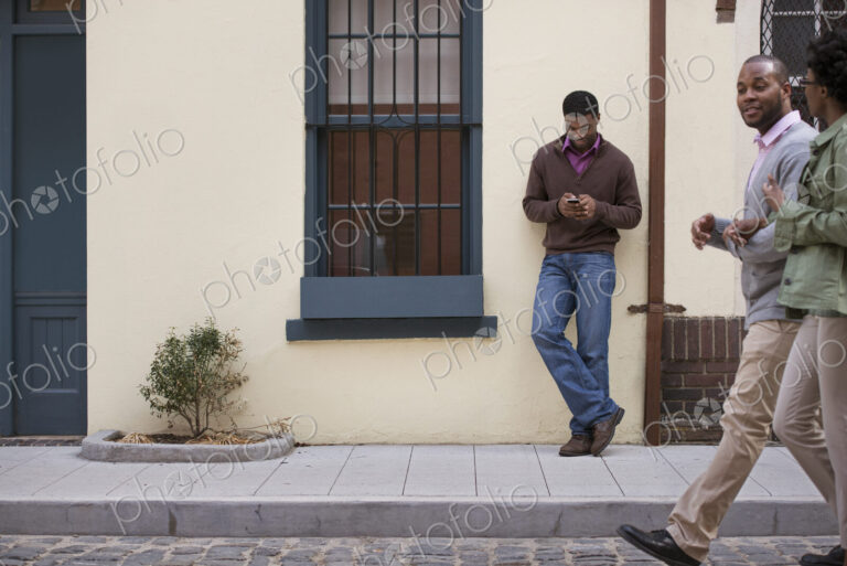 Outdoors in the city in spring. A couple walking on the sidewalk, and a man leaning…