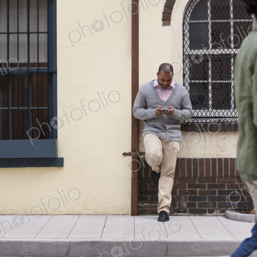 Outdoors in the city in spring. A couple walking on the sidewalk, and a man leaning… Outdoors in the city in spring. A couple walking on the sidewalk, and a man leaning…