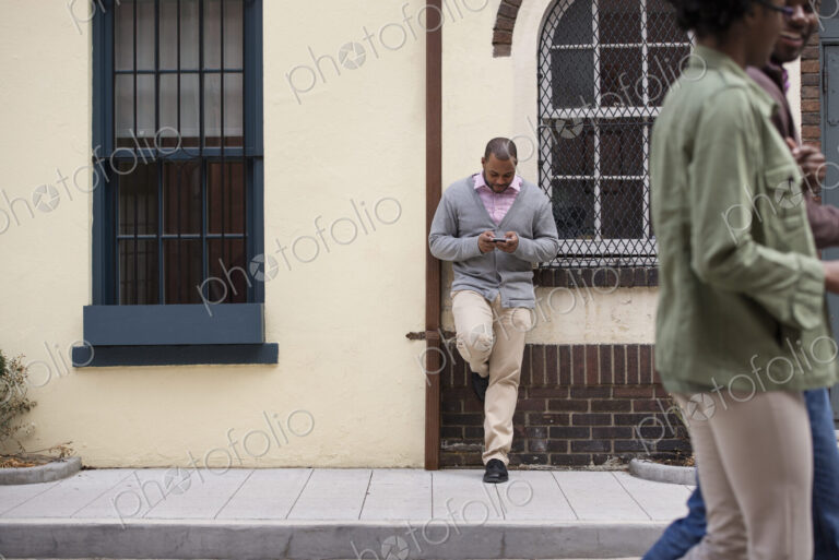 Outdoors in the city in spring. A couple walking on the sidewalk, and a man leaning…