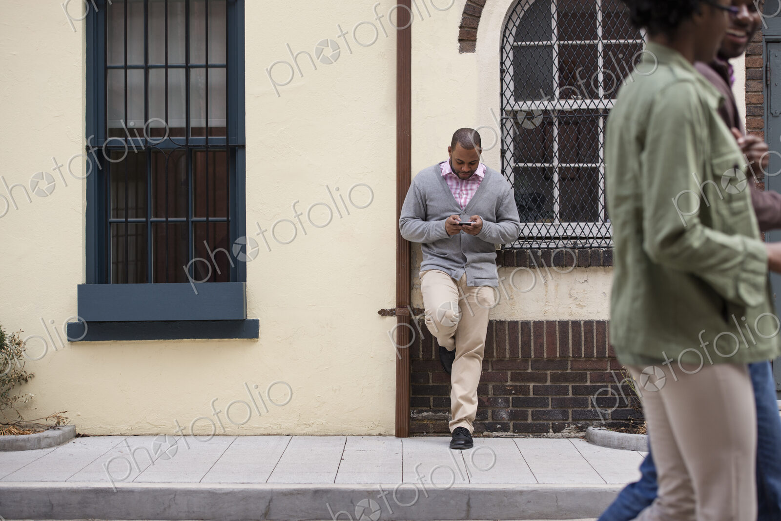 Outdoors in the city in spring. A couple walking on the sidewalk, and a man leaning…