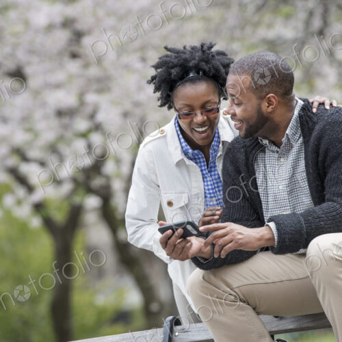 Outdoors in the city in spring. An urban lifestyle. A couple sitting on a bench, one…
