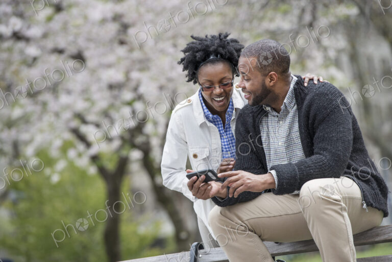 Outdoors in the city in spring. An urban lifestyle. A couple sitting on a bench, one…