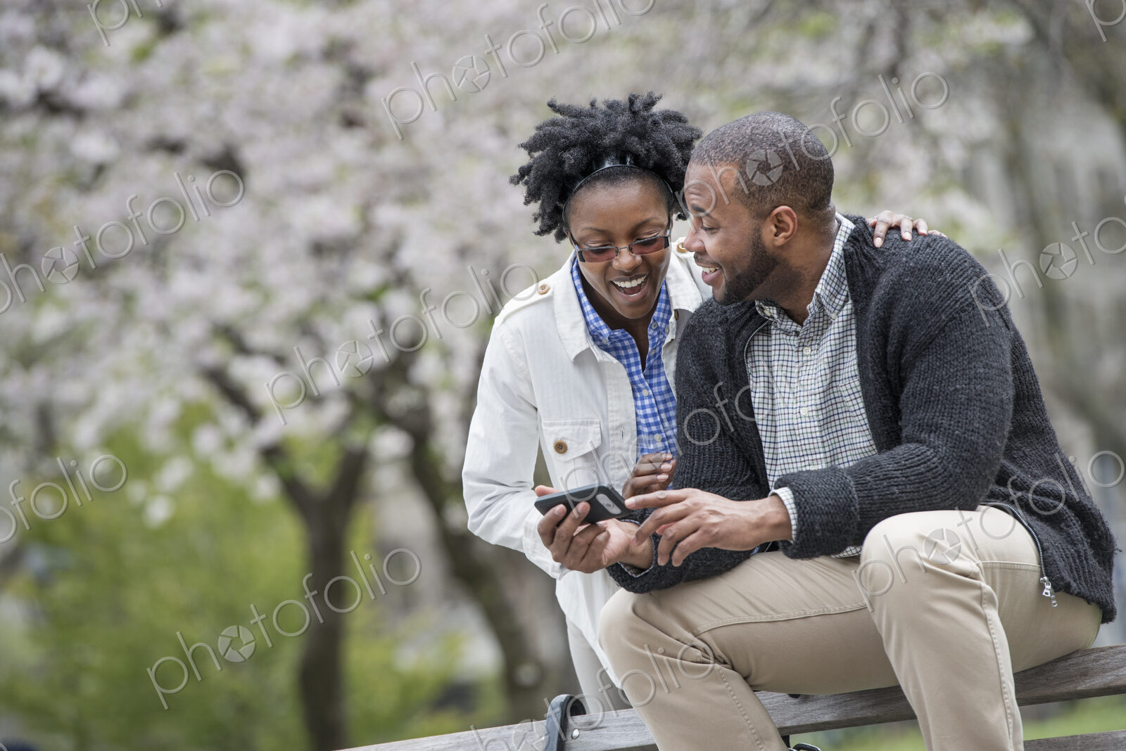 Outdoors in the city in spring. An urban lifestyle. A couple sitting on a bench, one…
